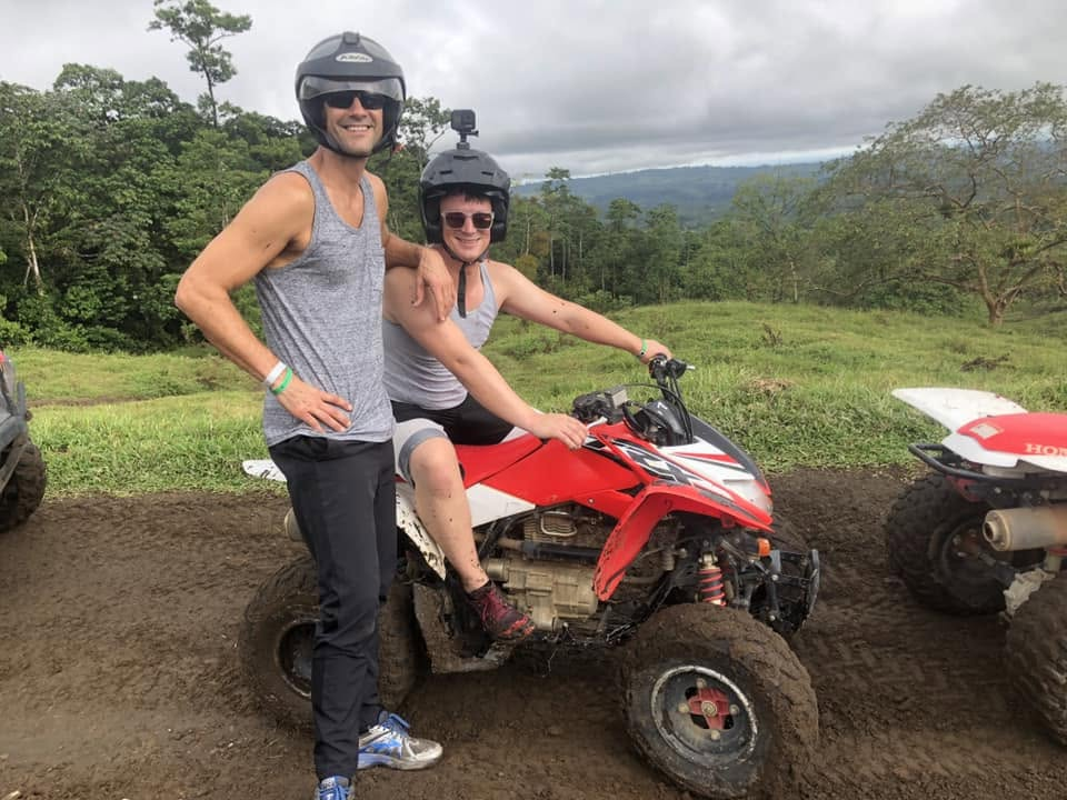 Two retreat guests in helmets beside a red ATV on a jungle trail